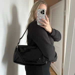 Axelremsväska - Lite större axelremsväska från Mango. Snyggt lackat material, rymlig då den är lite större. Bandet kan göras längre och kortare så du kan bära den på olika sätt. 