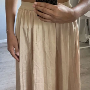 Grunt champagnefärgad långkjol. -  Kjolen är i storlek (S) och är tillverkad av högkvalitativt material som gör att den känns mjuk och behaglig mot huden. Den har en elegant champagnefärg och är lång, vilket gör den perfekt för finare tillfällen som bröllop, sommar fest eller bal.