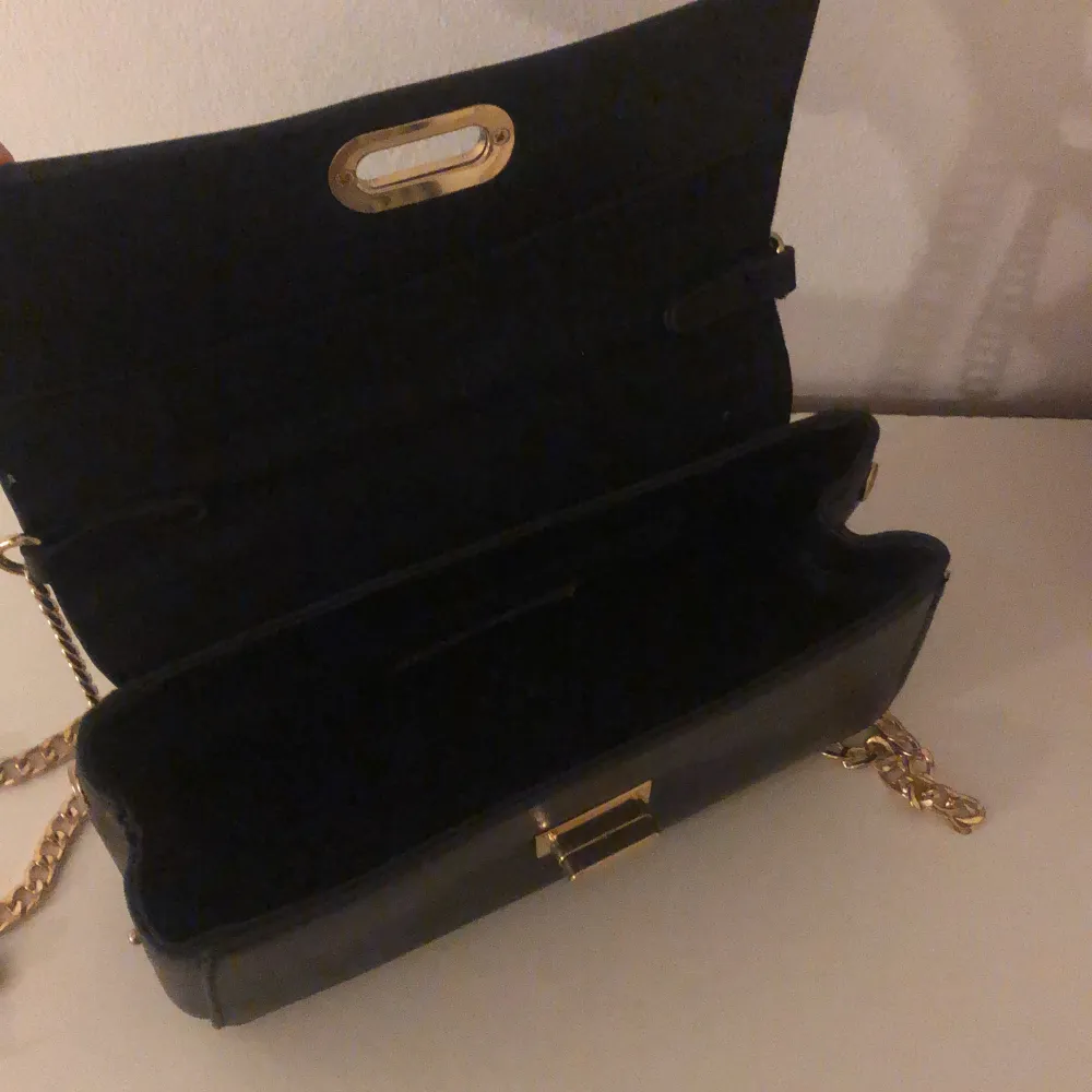 En liten svart handväska med guldigt kedjeband. Aldrig använd. Väskor.