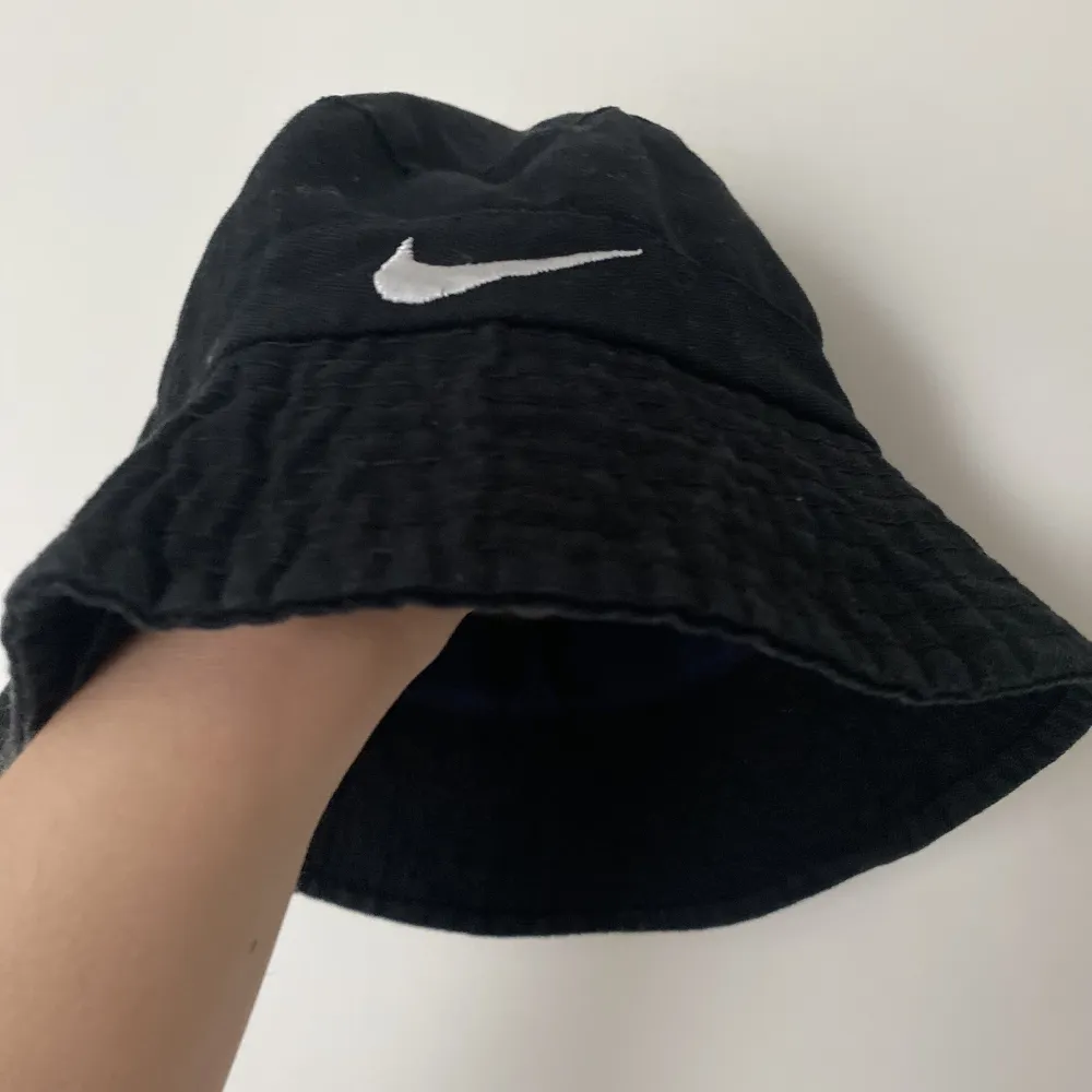 En svart buckethat/fiskarhatt med Nike logga bak och fram. Köpt secondhand, säljes då den är för liten. Har inga exakta mått men uppskattar att inreomfåget är drygt 48cm.  OBS Se bild 2, något tyg på insidan har lossnat lite. . Övrigt.