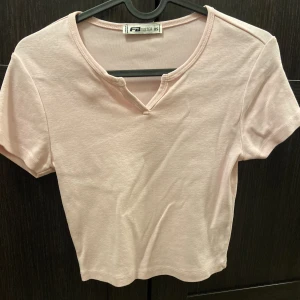 Kort rosa T-shirt med slits - I storlek xs. Har knappt använt tröjan. Nästan en magtröja. En fin detalj på tröjan är slitsen framtill där tröjan går från en vanlig T-shirt till något extra. En perfekt tröja för en fin hemmaoutfit likväl en tjejmiddag eller när du ska titta på barbie!