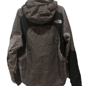The North Face windbreaker grå - En bra och skön jacka från The North Face. Varmare än en vanlig windbreaker. Inga defekter, endast använts en säsong. Lite skrynklig då den legat i garderoben, men är upphängd just nu och kommer att återgå till som vanligt. Läs min bio