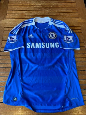 Chelsea fotbollströja (retro) - Detta är Chelseas hemmatröja ifrån säsongen 11/12 alltså säsongen dom vann Champions League! På ryggen är Juan Mata som då var en av Prems bästa. Skick: 9/10 Storlek: Large (?) Mått: nacke till mudd: 73 cm, armhåla-armhåla 55 cm 