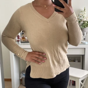 Stickad tröja - Fin beige stickad tröja, med guldiga knappar på ärmarna. Cuts på sidorna av tröjan. Storlek 2XS men passar som storlek S/M. 