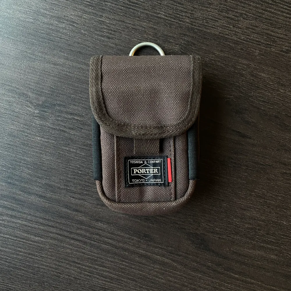 En liten brun pouch/coin purse från japanska märket Porter Yoshida  Väskan har brun färg med insida och resorband i cream färg.   Går att fästa till remmen i andra väskor som accessoar.  Som i nyskick!. Väskor.