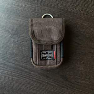 En liten brun pouch/coin purse från japanska märket Porter Yoshida  Väskan har brun färg med insida och resorband i cream färg.   Går att fästa till remmen i andra väskor som accessoar.  Som i nyskick!