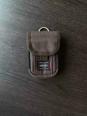En liten brun pouch/coin purse från japanska märket Porter Yoshida  Väskan har brun färg med insida och resorband i cream färg.   Går att fästa till remmen i andra väskor som accessoar.  Som i nyskick!