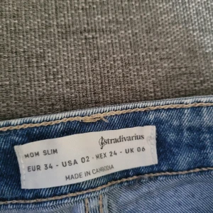 Blåa jeans stradivarius - Blå jeans i modellen mom slim storlek 34. Från stradivarius. På 3 bilden är det ett veck på knäet så inget trasigt.