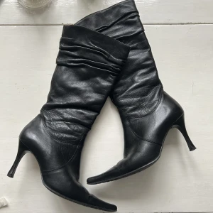 svarta stövlar med spetsig tå och klack - så snygga vintage svarta stövlar med klack och spetsig tå, i 37. skaftet är typ mid calf och har skitfina rynkade detaljer högst upp. köpta secondhand, finns inget märke men de är av tjockt äkta läder och i så bra skick ﾐ☆ skriv i chatten för frågor! PoK