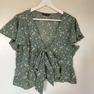 Blus  - En grön blus med vita blommor. Kort variant och skönt material. Med knytning i midjan. Storlek XL men jag har M och kan ha den.  Fin till sommaren!