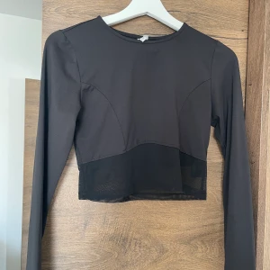 Träningstopp - Svart träningstopp med mesh tyg längst midjan, storlek M köpt på Nelly 