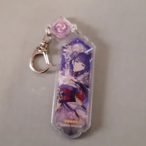 Raiden shougun keychain - Selling my raiden shougun keychain beacuse im no longer a fan of the game. I bougyt it at a con and had it on my bad for 2 days so no damage and its in the condition it was when i bought it! 3×12cm+chain. Contact me if u have any questions!💜⚡