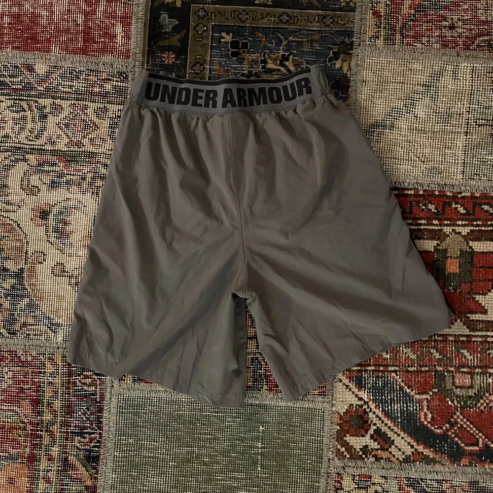 Säljer dessa gråa Under Armour träningsshorts i storlek medium med en skön loose fit passform. Perfekta för träning eller en avslappnad dag. De är i fint skick och väntar på en ny ägare!. Shorts.