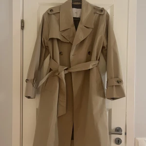 Beige Trenchcoat  - Säljer min långa trenchcoat från mango. Aldrig använt alltså i helt nyskick, säljer pga inte min stil då jag köpte enbart för att den är snygg I storlek Xs men passar även S Nypris 999kr mitt pris 550 + frakt men öppen för förslag
