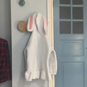 Tjocktröja/jacka med kaninöron - En lång vit tjocktröja/jacka med kaninöron på ca. 33,5 cm. Bysten är 101 cm, ärmarna 50cm, längd 72,5 cm. Snörena vid luvan är lite trasiga men annars är den toppen för hösten, vintern & våren. 