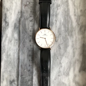 Daniel Wellington-klocka - Klocka med svart läderband och gulddetaljer. Köpt begagnad för några år sedan. Använt skick. Nytt batteri behövs! 