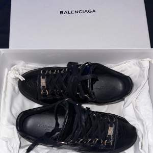 Svarta skor med guldiga detaljer från märket BALENCIAGA. De är i storlek 36(lite små) Väldigt fint skick, är bara använda ett fåtal gånger så nästan inga slitningar alls. Köpta för 5.400kr Kom privat för fler bilder då man endast kunde ha 3st