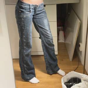 Skitnygga Lowwaist jeans med coola detaljer. De är omsydda till Lowwaist, men det syns inte. Uppsprättade längste ner och saknartyvärr knapp, därmed det låga priset Midjemått: 35cm Innerbenslängd: 75 cm Vidd längst ner: 24 cm