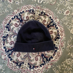 Tommy hilfiger Beanie  - Tja säljer nu denna as snygga mössa från Tommy hilfiger. Skick 9/10 endast använd någon enstaka gång. Perfekt nu under vintern. Hör av dig vid frågor eller funderingar!
