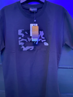 Amporio Armani - Säljer denna Amporio Armani T-shirten som är i svart färg och är storlek L och passar även för M den är liten i storlek.