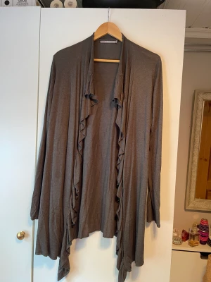 Kofta  - Grå kofta med volanger. Storlek: L. 