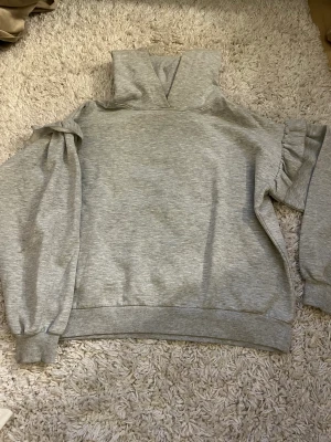 Grå hoodie - Söt grå hoodie från Primark, i storlek xs. Har gulliga små volang detaljer precis under axlarna som ger lite Stockholmsstil. Köpt för 300kr och använd under 5 gånger.