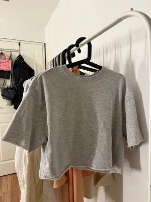 Grå croppad t-shirt från Zara - Säljer en basic grå sweatshirt t-shirt med trekvarts ärmar. Jättesnygg till blåa jeans! 