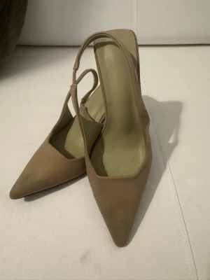 Beige spetsiga pumps med rem - Säljer ett par stilrena pumps i grön med spetsig tå och smal rem över foten.