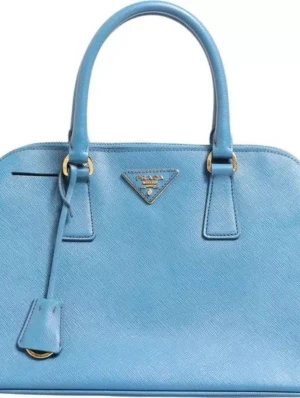 Blå handväska i läder från Prada - Snygg blå handväska från Prada i strukturerat läder med guldfärgade metalldetaljer. Väskan har två handtag, dragkedja upptill och en klassisk trekantig Prada-logga framtill. Perfekt för dig som vill ha en stilren och lyxig accessoar. 0684