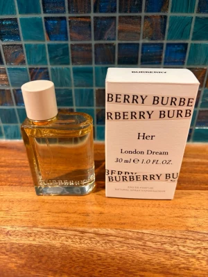 Burberry London Dream, edp 30ml - Burberry London Dream, edp, 30ml, endast använd ett par ggr, som ny! Säljer en elegant parfym i en rektangulär glasflaska med vit kork. Doften har fräscha toppnoter av citron och ingefära, blommiga hjärtnoter av pion och ros samt basnoter av mysk och amber. Flaskan är genomskinlig och stilren, perfekt för dig som gillar fräscha och blommiga dofter.
