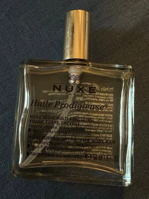 Nuxe Huile Prodigieuse torr olja - Multifunktionell torr olja i glasflaska med guldfärgad spraykork. Innehåller växtoljor som arganolja och ger näring, lyster och skydd till hud och hår. Passar alla hud- och hårtyper och har en fräsch doft. Perfekt för både kropp och hår.