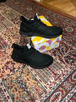 Ultraboost - Säljer ett par helsvarta Adidas Ultraboost sneakers med stickad ovandel och klassiska tre ränder på sidan. Skorna har en bekväm Boost-sula och Continental-gummiyttersula för extra grepp. Perfekta för dig som gillar stilrena och sportiga sneakers.