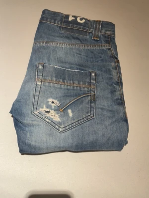 Ljusblå slitna jeans från dondup W30 L32 - Säljer ett par ljusblå jeans med raka ben och slitningar på bakfickorna. Jeansen har klassisk femficksdesign och tydliga slitdetaljer som ger en cool och avslappnad look. Perfekta för dig som gillar en trendig streetstil.