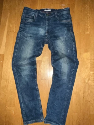 Mörkblå slim fit jeans - Snygga mörkblå jeans med slitningar och tvättade detaljer. Modellen är slim fit med normalhög midja och klassiska fem fickor. Jeansen har knappgylf och är i stretchigt material för extra komfort.