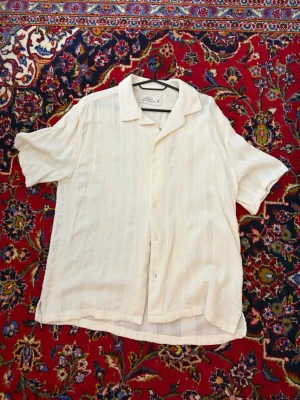 Vit linneskjorta från Abercrombie & Fitch - Säljer en luftig vit skjorta från Abercrombie & Fitch i linnemix. Skjortan har korta ärmar, klassisk krage och knappar framtill. Perfekt för sommaren med sitt tunna material och avslappnade passform.