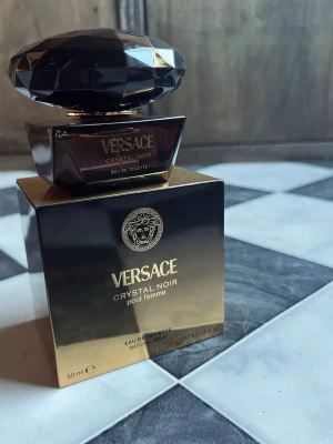  Versace Crystal Noir EdT, 50ml  - Versace Crystal Noir pour femme är en lyxig parfym i en elegant, mörklila flaska med diamantformad kork. Doften är sensuell och exklusiv, perfekt för dig som vill sticka ut. Flaskan rymmer 50 ml och kommer i en svart och guld ask.Den är helt ny!
