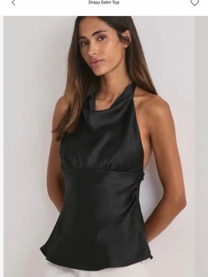 Svart halterneck topp i satin - Säljer en svart halterneck topp i glansigt satinmaterial. Toppen har en draperad halsringning och är ärmlös med öppen rygg. Då jag har flertal liknande toppar hemma 