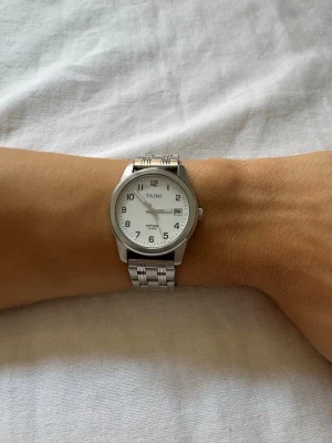  TAIMS klocka, läs beskrivning! - TAJMS vit herrklocka med datumfunktion. På uret står det ”Sapphire” och ”10 ATM”.   Uret mäter 36 mm i diameter  Klockan TICKAR INTE, men i övrigt mycket bra skick. Möjligtvis behöver den endast ett nytt batteri. 
