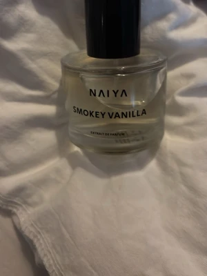 Naiya Smokey Vanilla Parfym - Upptäck Naiya Smokey Vanilla, en elegant parfym i en rund, genomskinlig glasflaska med svart kork. Doften bjuder på en unik mix av rökig vanilj som känns både modern och mysig. Perfekt för dig som gillar subtila men karaktärsfulla dofter.