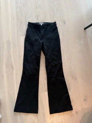 Svarta bootcut byxor - Säljer ett par svarta bootcut byxor med hög midja och utsvängda ben. Byxorna har en enkel design utan synliga fickor eller detaljer och är perfekta för en trendig och stilren look. Materialet ser ut att vara mjukt och stretchigt.