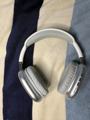 Stora over-ear hörlurar i silver - Snygga over-ear hörlurar i silver och vitt med mjuka, vadderade öronkuddar och justerbart huvudband. Hörlurarna har flera knappar på sidan och medföljer en vit sladd med 3,5 mm kontakt. Perfekta för musik, gaming eller film.