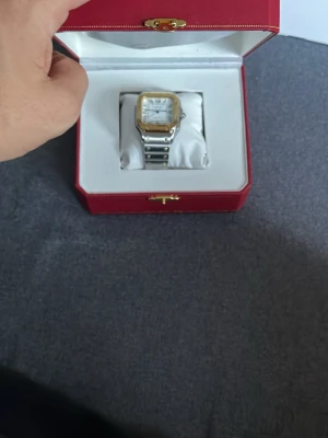 Stilren tvåtonad fyrkantig klocka - Säljer en elegant klocka i silver och guldton med fyrkantig urtavla och romerska siffror. Armbandet är i metall med synliga skruvar och klockan levereras i en röd lyxig ask. Perfekt accessoar för dig som gillar klassisk och tidlös design.