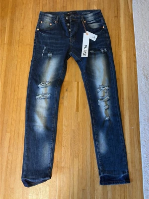 Blå slitna skinny jeans från Purple - Säljer ett par blå skinny jeans från Purple med slitningar och distressed detaljer på framsidan. Jeansen har klassisk femficksmodell, knappgylf och snygg tvätt med ljusa partier. Perfekta för en trendig och avslappnad look.