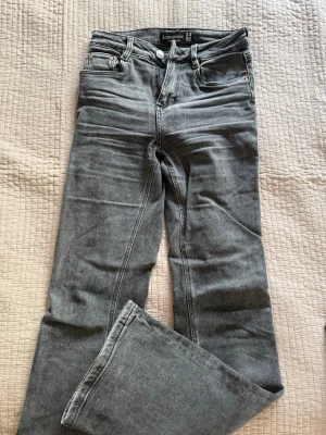 Grå raka jeans från Stradivarius - Säljer ett par grå jeans från Stradivarius i rak modell. Jeansen har klassisk femficksdesign, bälteshällor och knappgylf. Materialet är denim med en tvättad look som ger en avslappnad vibe. Perfekta till sneakers eller boots.