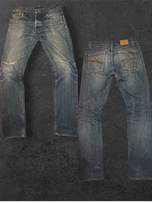 Sinnessjuka vintage Nudie Jeans - Säljer ett par blå jeans med slitningar och lagade hål på knäna. Jeansen har raka ben, klassisk femficksmodell och kontrastsömmar. Materialet är denim i bomull och bakfickorna har dekorativa sömmar. Ett hål i fickan fråga gärna om de