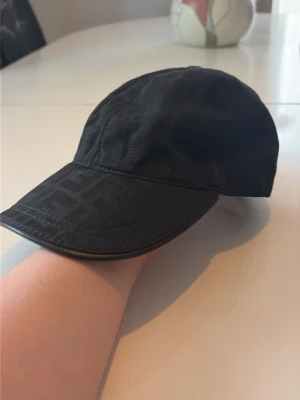 Svart keps med ton-i-ton-mönster - Snygg svart keps med diskret ton-i-ton-mönster på skärmen och framsidan. Klassisk böjd skärm och justerbar passform. Tillverkad i ett slitstarkt tyg som ger en stilren och modern look. 