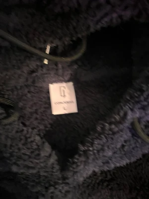 Mörkblå fluffig hoodie Common Sense - Mysig och oversized mörkblå hoodie från Common Sense i fluffigt teddy-material. Hoodien har en stor huva med dragsko och en liten patch på bröstet. Perfekt för dig som gillar streetwear och vill ha något riktigt bekvämt.