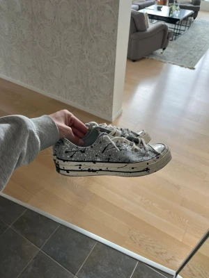 Converse chuck Taylor - Unika vita sneakers med svart stänkmönster och vita snören. Klassisk låg modell med gummisula och canvasmaterial. Perfekta för dig som vill sticka ut med en kreativ och cool stil. Converse chuck Taylor paint splatter