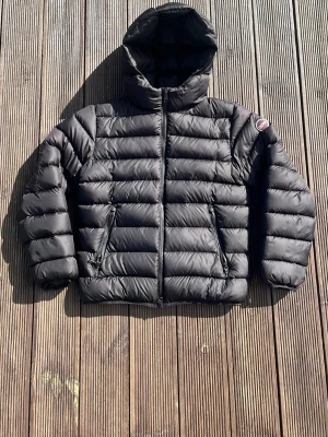 Svart dunjacka från Colmar - Snygg svart dunjacka från Colmar med huva och två dragkedjeförsedda fickor. Jackan har ett quiltat mönster och Colmar-logga på ärmen. Perfekt för kalla vinterdagar och riktigt skön att bära. Storlek 154