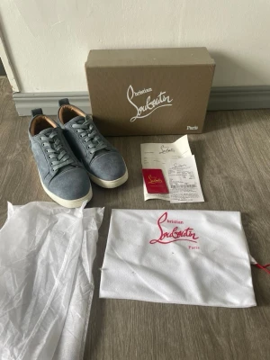 Gråa sneakers från Christian Louboutin - Snygga gråa sneakers från Christian Louboutin i mocka med vita sulor och matchande grå skosnören. Skorna har en klassisk låg siluett och detaljer i läder på insidan. Perfekta för dig som vill ha en exklusiv touch på din outfit.